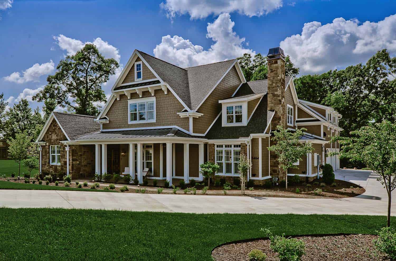 Craftsman style custom home with stone, covered porch and steep gables under a blue sky